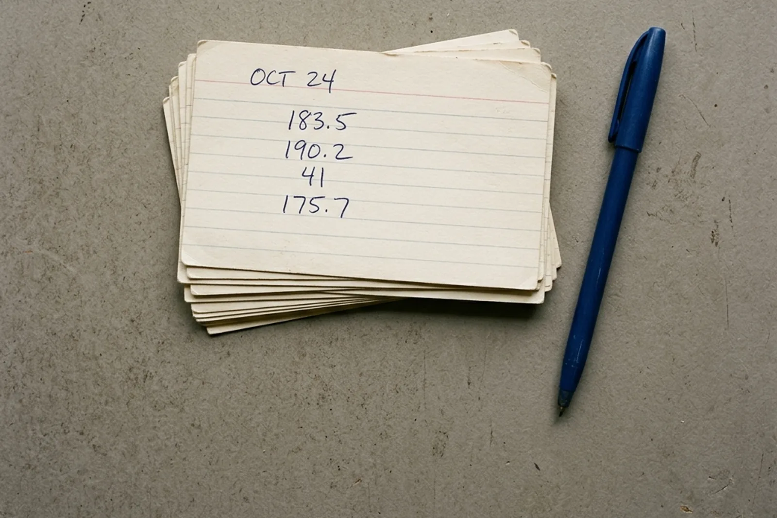 A stack of handwritten index cards and a pen on a grey surface.